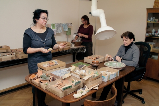 grupa osób w pracowni konserwacji zabytków archeologicznych, na stole pudełak z obiektami zabytkowymi
